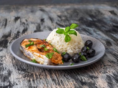 Pirinç ve balıkla öğle yemeği, zeytin ve yeşil fesleğen, yakın plan gri bir tabakta servis edilir.