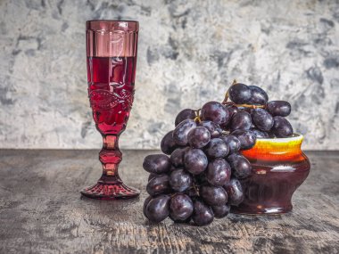 Hoş bir akşam için pembe cam kadehte bir demet siyah üzüm ve kırmızı şarap.