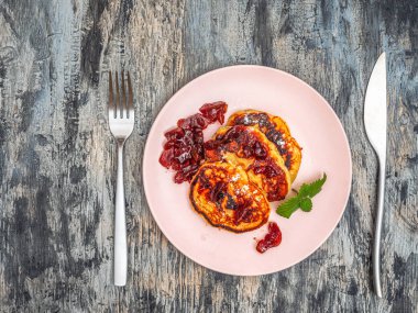 Elma reçelli krep ve pembe tabakta pudra şekeri ve gri arka planda çatal bıçak takımı.