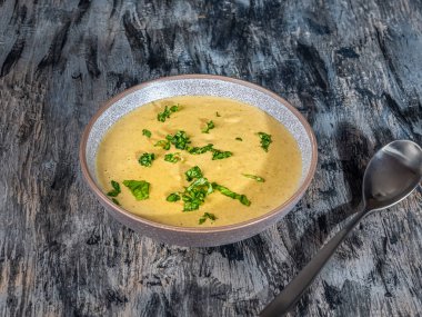 Derin bir tabakta fesleğen çorbası ve yakın plan gri-siyah bir yemek kaşığı.