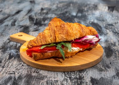 Jambonlu, peynirli, yeşil salatalı ve domatesli kruvasan sandviçi, ahşap bir tahtanın üzerinde servis edilir.