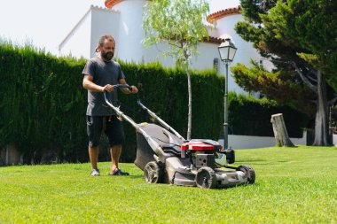 Erkek bahçıvan çimen biçiyor arka bahçede modern çim biçme makinesiyle bahçenin bahçesinde mevsimlik bakımını yapıyor profesyonel bahçe bakımını yapıyor.