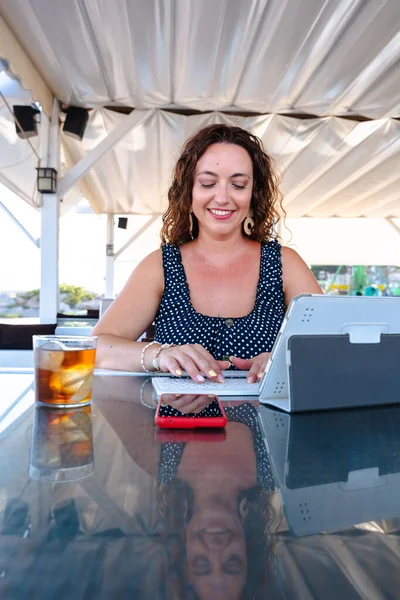 Açık kafedeki terasta dijital tablette çalışan gülümseyen kadın ferahlatıcı, modern yaşam tarzı uzaktan çalışma, teknoloji kullanımı ve profesyonel üretkenlik kavramına sahip. Dikey