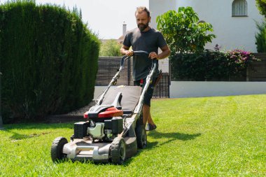 Erkek bahçıvan çimen biçiyor arka bahçede modern çim biçme makinesiyle bahçenin bahçesinde mevsimlik bakımını yapıyor profesyonel bahçe bakımını yapıyor.