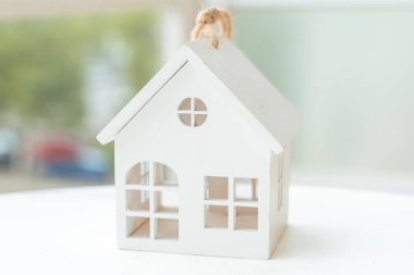 Bulanık arka plan ve yumuşak gün ışığıyla parlak bir masaya yerleştirilmiş en az beyaz ev modeli. Konut, mülk, güvenlik, mimari, basitlik, ipotek, mülkiyet ve emlak yatırımı kavramı.