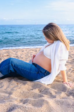 Hamile kadın kumsalda dinleniyor, sakin mavi deniz ufkuna bakıyor, annelik konsepti, bebek, huzur, doğa, sükunet, aşk, yaz, bağlantı sevinci, sakinlik,.