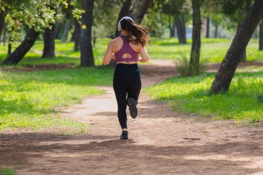 Spor kıyafetleri ve kulaklıklar takarak parkta tek başına koşan bir kadın, sağlıklı yaşam tarzı, özgürlük, enerji, motivasyon, eğitim, kararlılık ve aktivite kavramı..