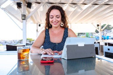 Açık kafedeki terasta dijital tablette çalışan gülümseyen kadın ferahlatıcı, modern yaşam tarzı konsepti uzaktan çalışma, teknoloji kullanımı ve profesyonel üretkenlik ile
