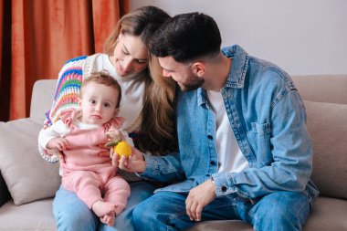 Mutlu genç ebeveynler evlerinde kanepede oturup bebek ile vakit geçiriyorlar, aile sevgisi, ebeveynlik, ilgi, çocukluk, birliktelik ve sıcak ve rahat bir atmosferde aile hayatı.