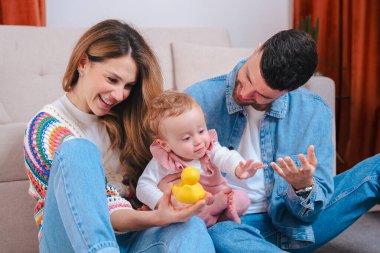Gülümseyen genç ebeveynler ellerinde sarı oyuncaklarla oynuyorlar, aile sevgisi, ebeveynlik, çocukluk, bakım, mutluluk ve neşeli duygularla rahat bir ev hayatı.