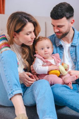 Gülümseyen genç ebeveynler ellerinde sarı oyuncaklarla oynuyorlar, aile sevgisi, ebeveynlik, çocukluk, ilgi, mutluluk ve neşeli ev hayatı.