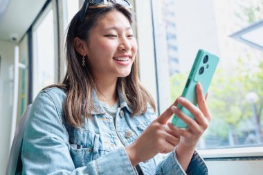 Heyecanlı kadın toplu taşıma araçlarında seyahat ederken akıllı telefon ekranına bakıyor. İnternette iyi haber ya da mesaj okuyan mutlu genç bayan, iletişimi, bağlantıyı, başarıyı simgeliyor.