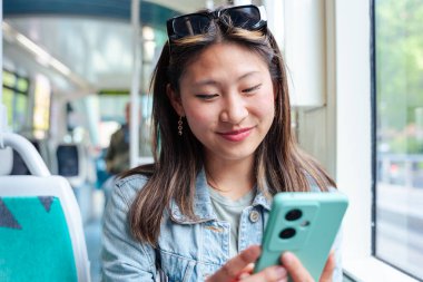 Heyecanlı kadın toplu taşıma araçlarında seyahat ederken akıllı telefon ekranına bakıyor. İnternette iyi haber ya da mesaj okuyan mutlu genç bayan, iletişimi, bağlantıyı, başarıyı simgeliyor.