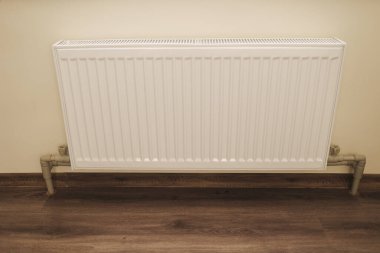  Ahşap zemini olan modern bir evin içindeki duvara sabitlenmiş beyaz radyatör. Isıtma ekipmanları, iç kısımlarda soğuk kış mevsiminde sıcaklık ve konfor sağlar. Yüksek kalite fotoğraf