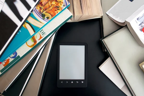 E-book with a gray screen on the black table among the many paper books