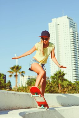 Bir kaykay üzerinde sürme ve güneşli havalarda hile yapma güzel kız