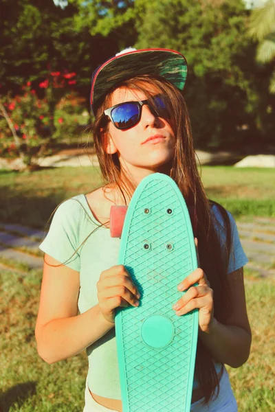 Menina adolescente bonita em óculos de sol com um skate em suas mãos — Fotografia de Stock