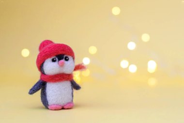 Noel oyuncağı, kışın kırmızı şapkalı ve eşarplı sevimli penguenleri bokeh 'li sarı arka planda hissetti.