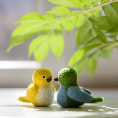 Güneşli bir günde yeşil yaprakların altında iki küçük oyuncak yünlü kuş. Kuru keçe