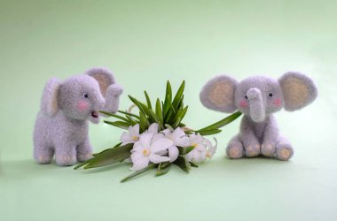 Yeşil arka planda beyaz çiçekli iki sevimli oyuncak fil. Kuru keçe.