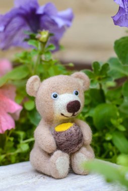 Oyuncak, el yapımı sevimli ayı çiçeklerin arasında bal fıçısıyla oturur, yün hisseder.