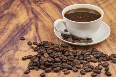 Kahve fincanı, ön planda. Fotokopi alanı olan, rustik ahşap bir masada taze kavrulmuş fasulye.