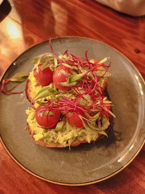 Avokado, fesleğen, lahana ve zeytinyağıyla süslenmiş kiraz domatesli kahvaltı sandviçi.