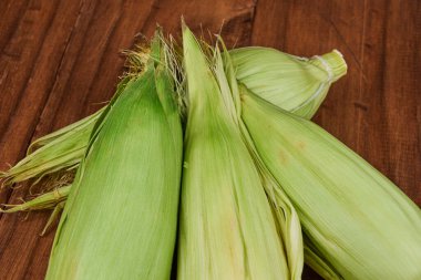 Yeşil kabuklar içinde taze mısırın kulakları ve kırsal ahşap arka planda ipek.