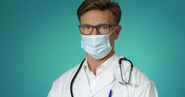 英俊男性医生头戴医用面罩的画像室内慢动作。人民与传染病。医疗工作者白色实验室外套和眼镜。医学概念. — 图库视频影像