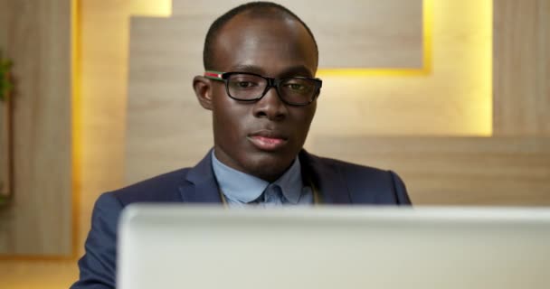 英俊而有思想的严肃的非洲裔美国青年商人坐在办公室与笔记本电脑寻找商业解决方案。超前近视的人物形象观念解决了问题的概念. — 图库视频影像