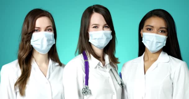 Hermosas mujeres jóvenes doctores que usan máscaras faciales médicas en interiores. Grupo Internacional de Personal Médico Femenino Profesional Confiado Posando en Abrigos Blancos Slow Motion Covid-19 Protection Health Care. — Vídeos de Stock