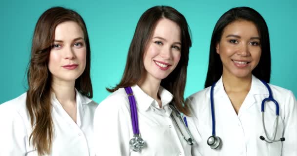 Hermosas chicas médicas en batas blancas sonriendo y posando en la cámara en interiores de cámara lenta. Grupo de mujeres jóvenes y felices Médicos Primer plano retrato de la cara. Concepto de Medicina Moderna y Salud. — Vídeos de Stock