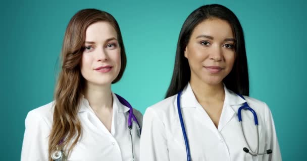 Beautiful Young Happy Medics Girls Smiling at Camera. Two Successful Confident Modern Female Doctors Posing in White Coats Slow Motion. Women Medicine Workers. Health Care and Medicine Concept. — Stock Video