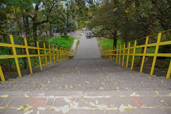 Long concrete staircase with yellow railings descending through autumn foliage.Concrete staircase with yellow railings descends through a park with autumn foliage. 