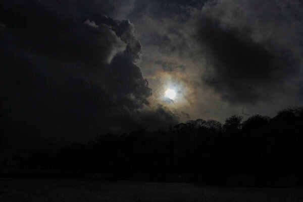 Sunlight breaks through dark clouds above the silhouette of trees.Sunlight filters through thick dark clouds, creating a striking contrast with the silhouette of the trees below. 