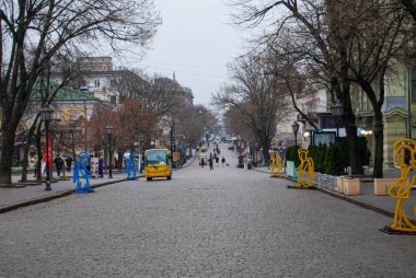 Yayalar ve heykellerle dolu kaldırımtaşı şehir sokağının uzun görüntüsü. Odessa 'da yapraksız ağaçlar ve klasik sokak lambalarıyla kaplı kaldırım taşı caddesi..
