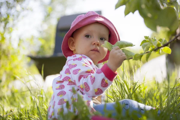 L'enfant s'assoit sur l'herbe et s'accroche à une brindille — Photo