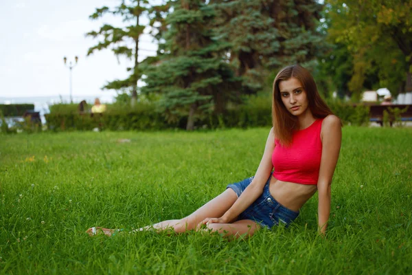 Menina esbelta senta-se no parque na grama — Fotografia de Stock
