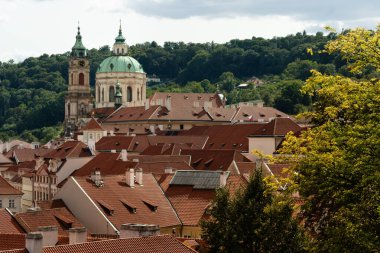 Mala Strana 'daki Aziz Nicholas Kilisesi Prag, Çek Cumhuriyeti' ndeki Castle Gardens terasında kırmızı çatıları ve Petrin Tepesi 'nin altında yaz bulutları altında görüldü..