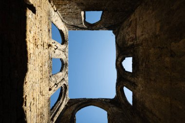 Almanya 'nın Saksonya kentindeki Oybin Dağı' ndaki şato kompleksinin bir parçası olan Oybin Manastırı 'nın güneş ışığındaki harabelerinde mavi gökyüzünü çerçeveleyen gotik kemerler.