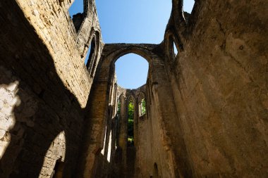 Almanya 'nın Saksonya kentindeki Oybin Dağı' ndaki şato kompleksinin bir parçası olan Oybin Manastırı 'nın güneş ışığındaki harabelerinde mavi gökyüzünü çerçeveleyen gotik kemerler.