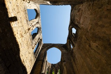 Almanya 'nın Saksonya kentindeki Oybin Dağı' ndaki şato kompleksinin bir parçası olan Oybin Manastırı 'nın güneş ışığındaki harabelerinde mavi gökyüzünü çerçeveleyen gotik kemerler.