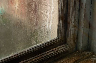 Buhar ve su damlacıkları eski bir ahşap çerçevenin sisli camında boyası soyulmuş.