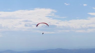 Bir adam gökyüzünde planörle uçuyor. Mavi gökyüzüne karşı rüzgar akıntılarını yakalıyor. Paragliding özgürlük, adrenalin ve bunu tekrar etme arzusudur..