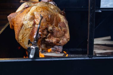Jambon yakın plan. Terbiye edilmiş et büyük bir barbeküde bahçede bir tükürükte kızartılır. Jambonun altın rengi, ısı ve duman yayan canlı bir ateş tarafından yaratılır. Turistler tarihi şehirlerde açık havada yemek yerler..