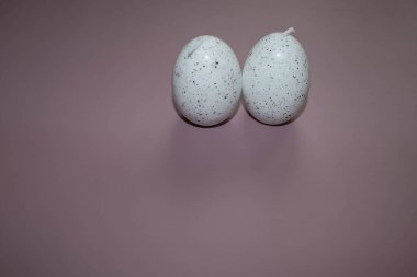 Yumurta şeklinde dekoratif Paskalya mumları. Dikey olarak pembe ya da eflatun arkaplana yerleştirilmiş. Mumlar beyaz bir temel renge sahiptir ve küçük siyah noktalarla kaplıdır. Paskalya süslemeleri olarak kullanılıyor.