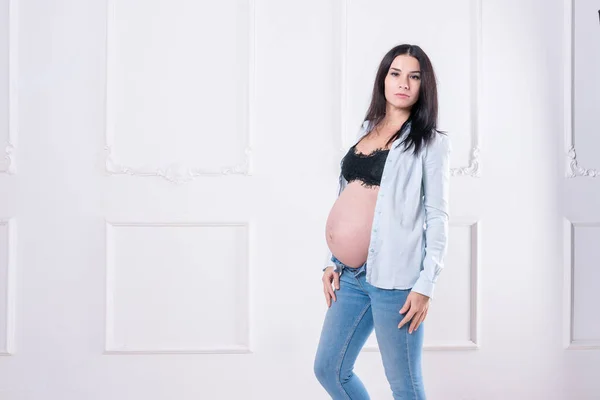 Zwanger meisje in jeans en een shirt. — Stockfoto