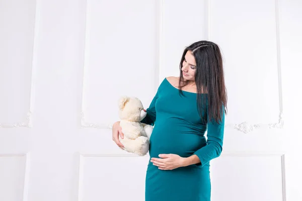 Беременная девушка в платье с плюшевым мишкой в руках. — стоковое фото