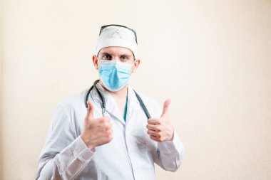 Maskeli ve şapkalı doktor, baş parmağını kaldırıyor..
