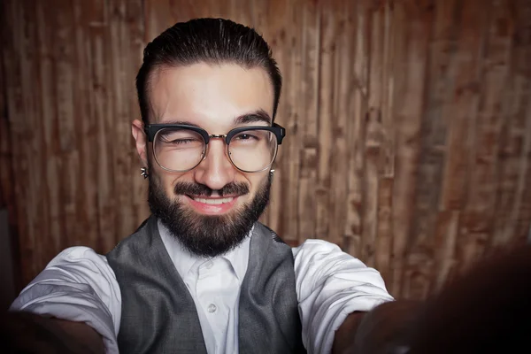 Divertente elegante giovane ragazzo facendo selfie su uno sfondo di legno — Foto Stock